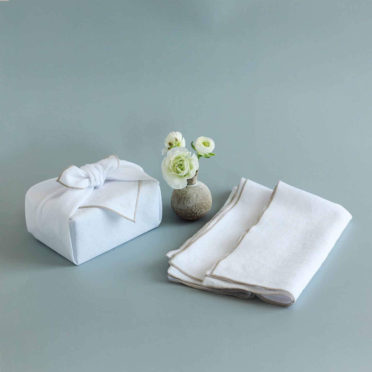White fabric wrapped gift with a vase of flowers on a gray background