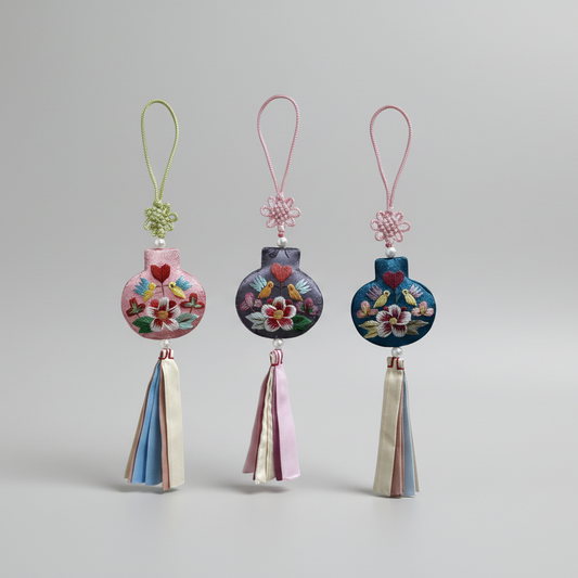Three decorative phone charms with floral designs and tassels on a white background