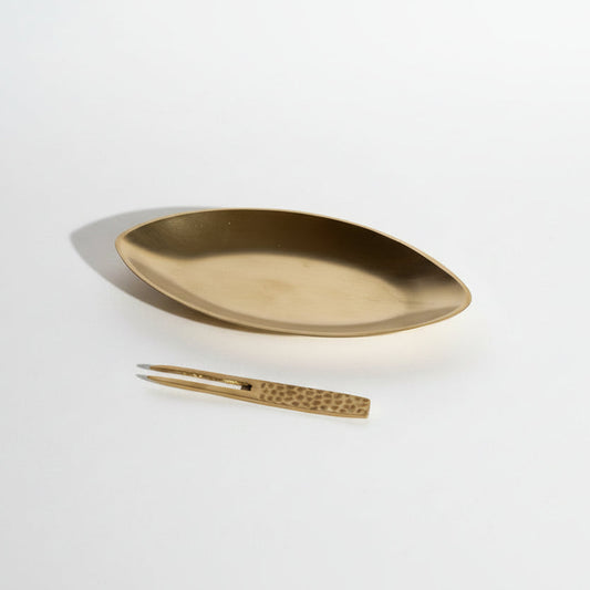 Gold oval dish and decorative item on a textured beige surface with shadows.